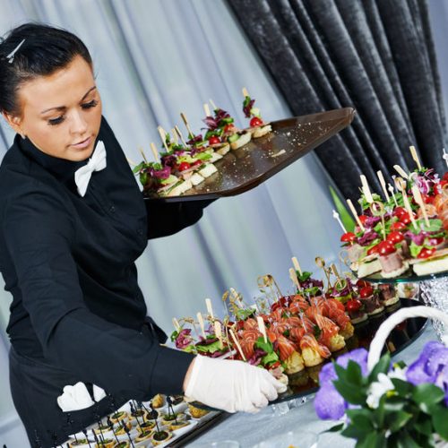 32615831 - waiter with meat dish serving catering table with food snacks during party event