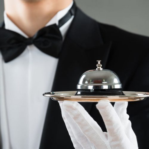 48645369 - midsection of waiter holding service bell in plate against gray background